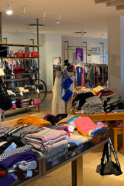 Ein Bekleidungsgeschäft mit Regalen voller Kleidung und Accessoires. Im Vordergrund liegt gefaltete Kleidung auf einem Tisch.