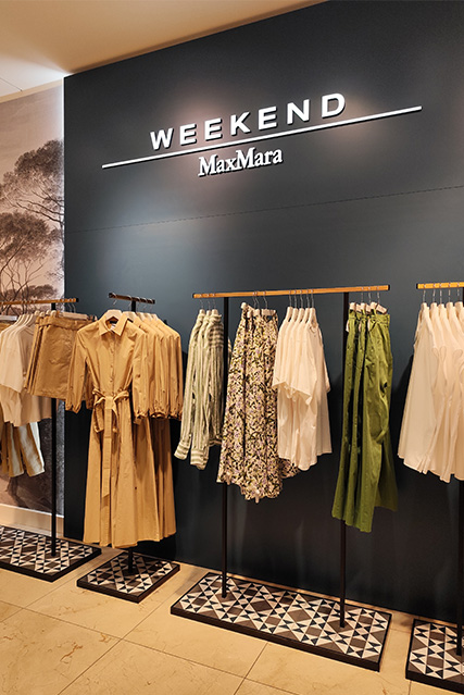 Kleiderständer mit verschiedenen Kleidungsstücken in einem Geschäft mit der Beschilderung "Weekend MaxMara".