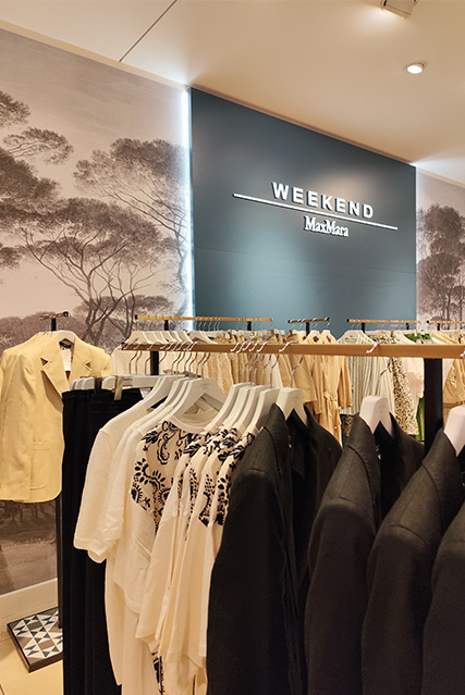 Kleiderständer mit Damenbekleidung in einem Geschäft, im Hintergrund ein Schild mit der Aufschrift "Weekend MaxMara".