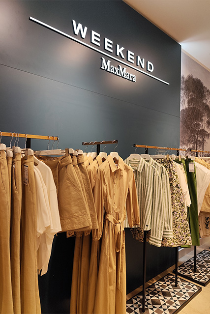 Kleiderständer in einem Geschäft von MaxMara Weekend mit hellen, natürlichen Stoffen und verschiedenen Kleidungsstücken.