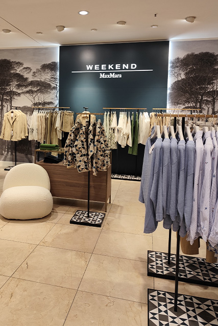 Ein Laden mit Kleidung der Marke "Weekend MaxMara"; beige, weiße und blaue Kleidungsstücke sind auf Kleiderständern ausgestellt, im Hintergrund ein großformatiges Naturbild.
