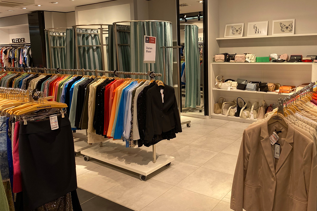 Das P&C Markenoutlet in Bremen mit Ständern voller bunter Jacken, einem Regal mit Accessoires und einer Umkleidekabine im Hintergrund.