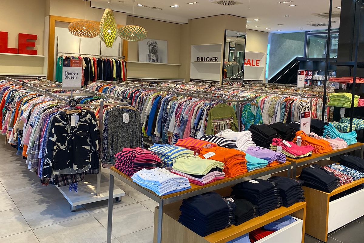 Das P&C Markenoutlet in Bremen mit Sale-Schildern, Kleiderständern voller bunter Damenblusen und einem Tisch mit ordentlich gefalteten T-Shirts in verschiedenen Farben.