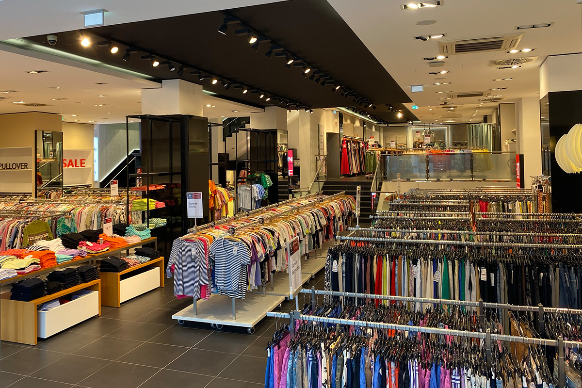 Das P&C Markenoutlet in Bremen mit mehreren Reihen von Kleidungsstücken auf Kleiderständern und Tischen, Schilder mit "Sale"-Hinweisen.